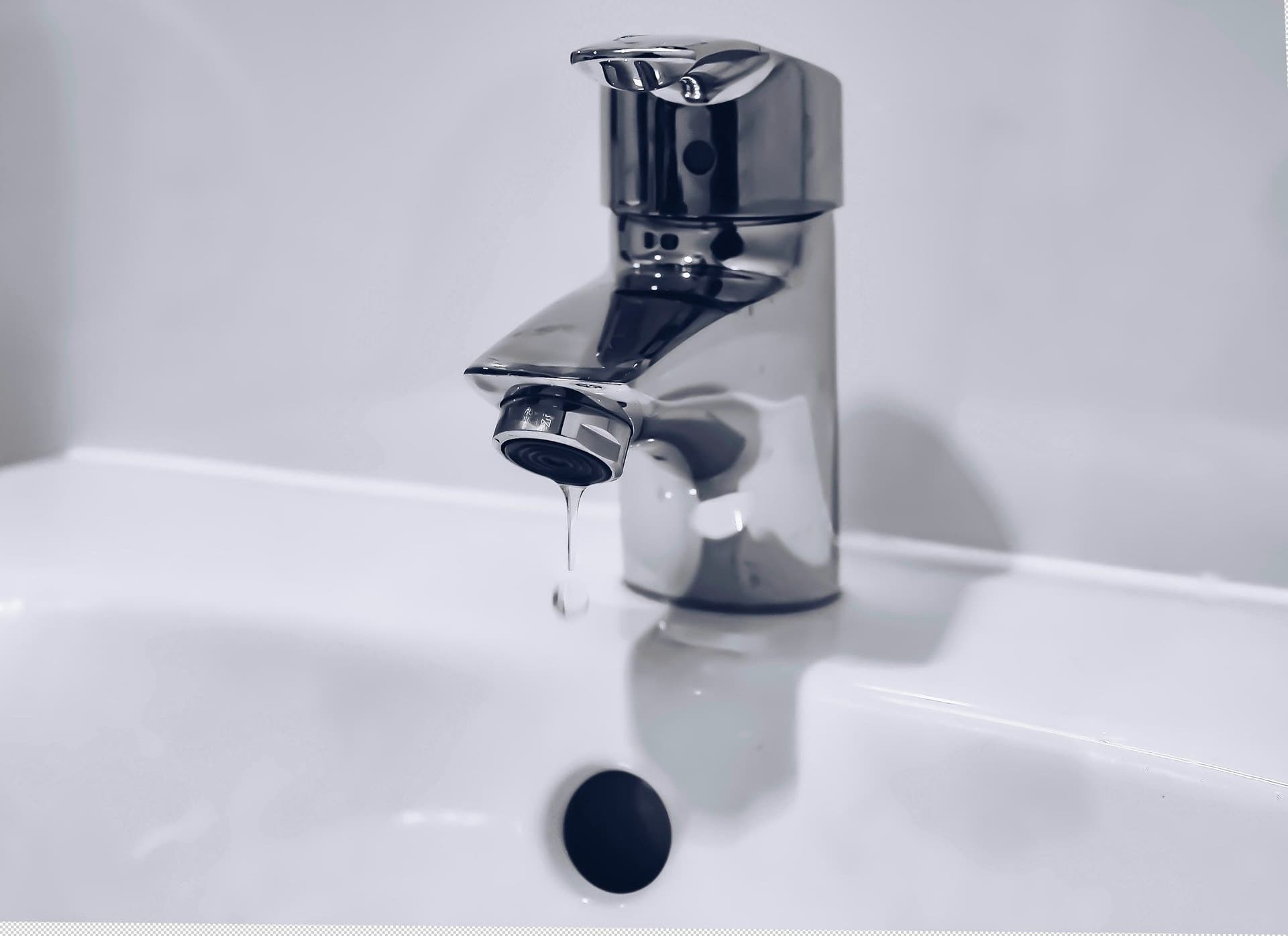 Chrome bathroom faucet with a single drop of water falling into a white sink