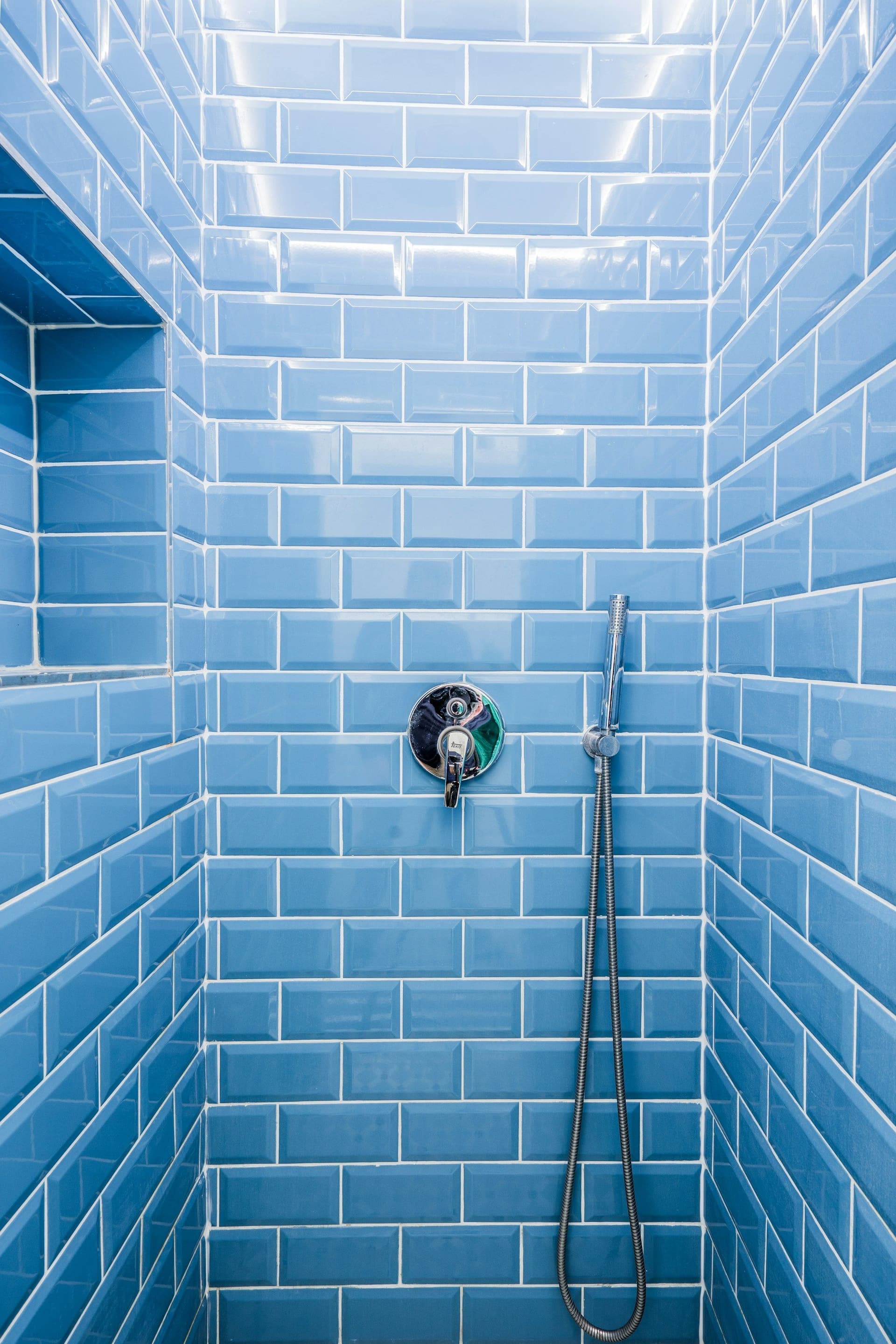 Shower enclosure fully tiled in glossy blue metro tiles, with a recessed niche and handheld shower