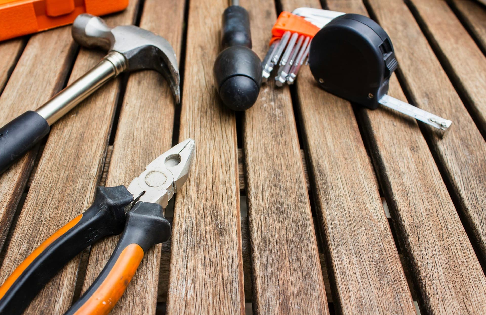A hammer, pliers, hex keys and a tape measure laid out on wooden decking