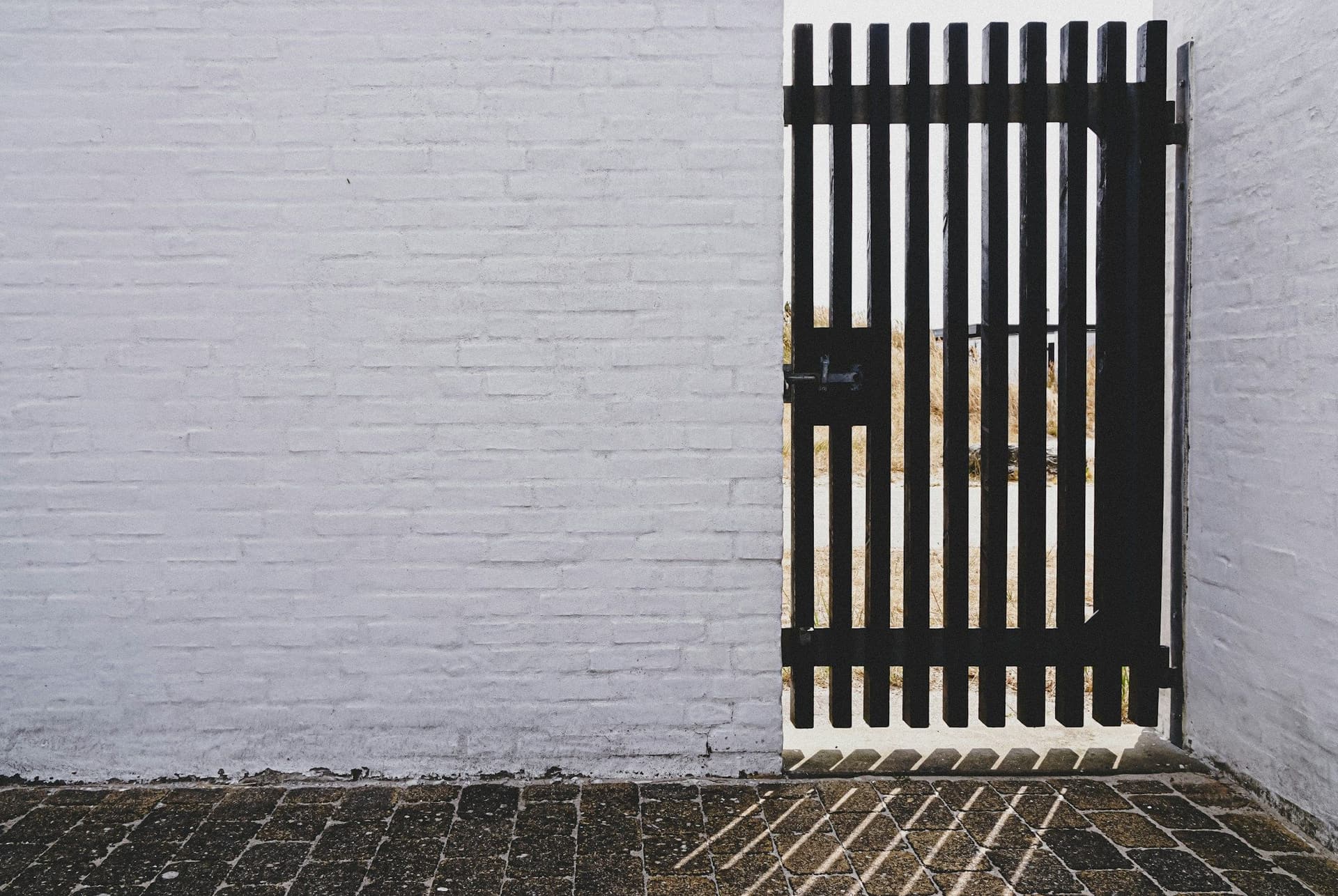 Black vertical-slat metal gate set into a white painted brick wall