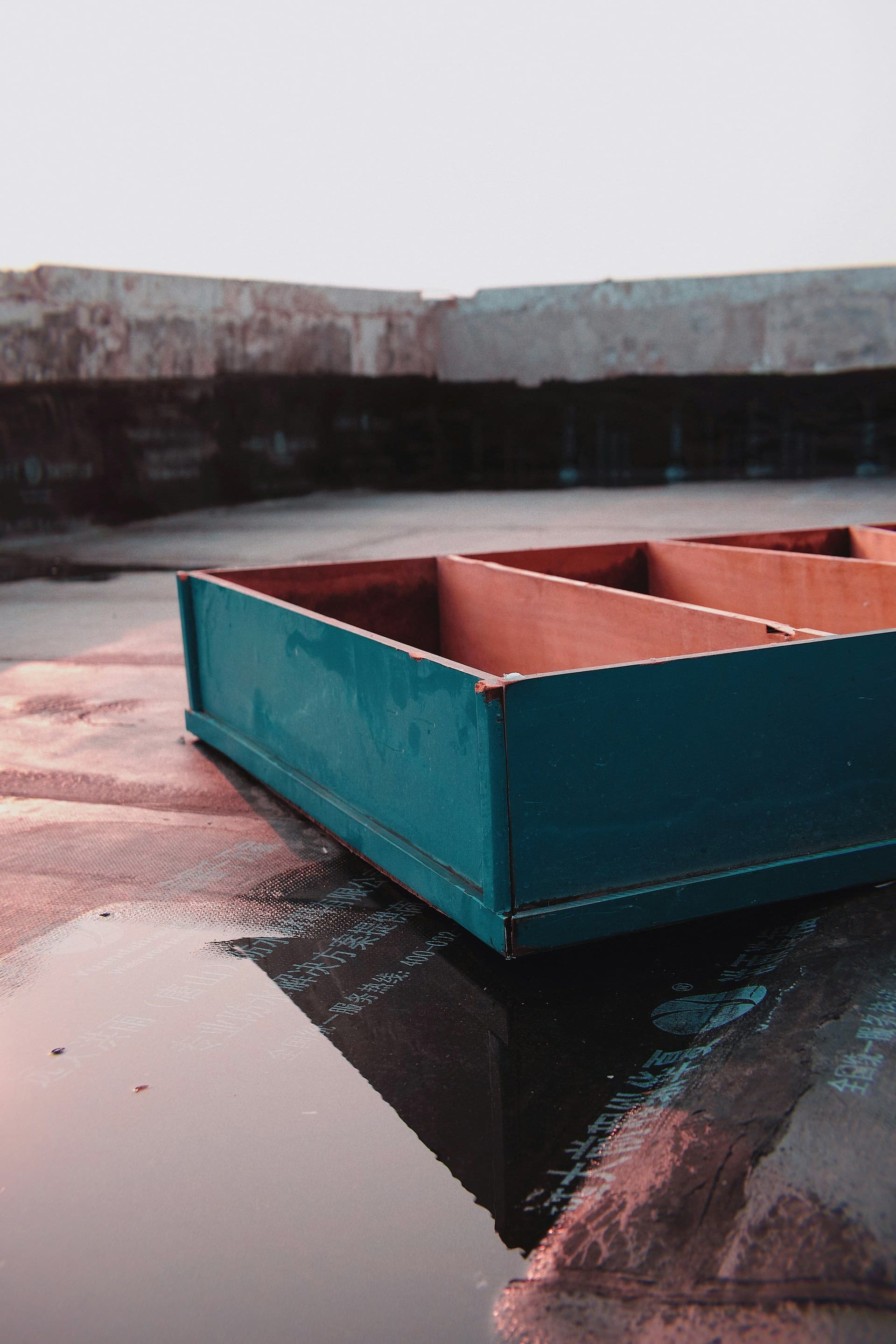 Rainwater pooled on a flat roof surface beside a teal rooftop metal box