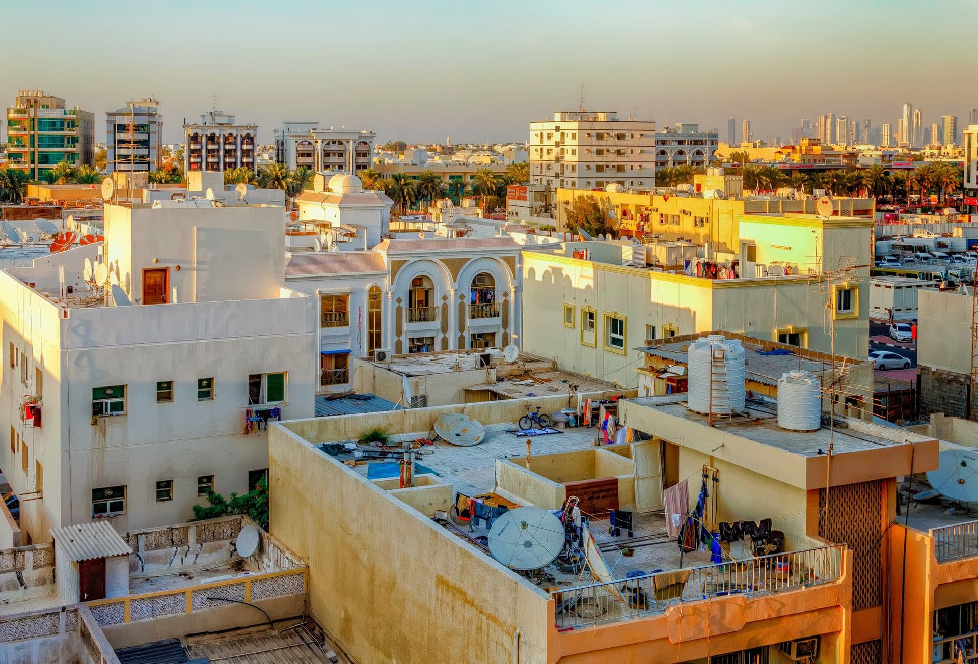 Flat rooftops with satellite dishes and water tanks on sand-colored apartment buildings in warm evening light