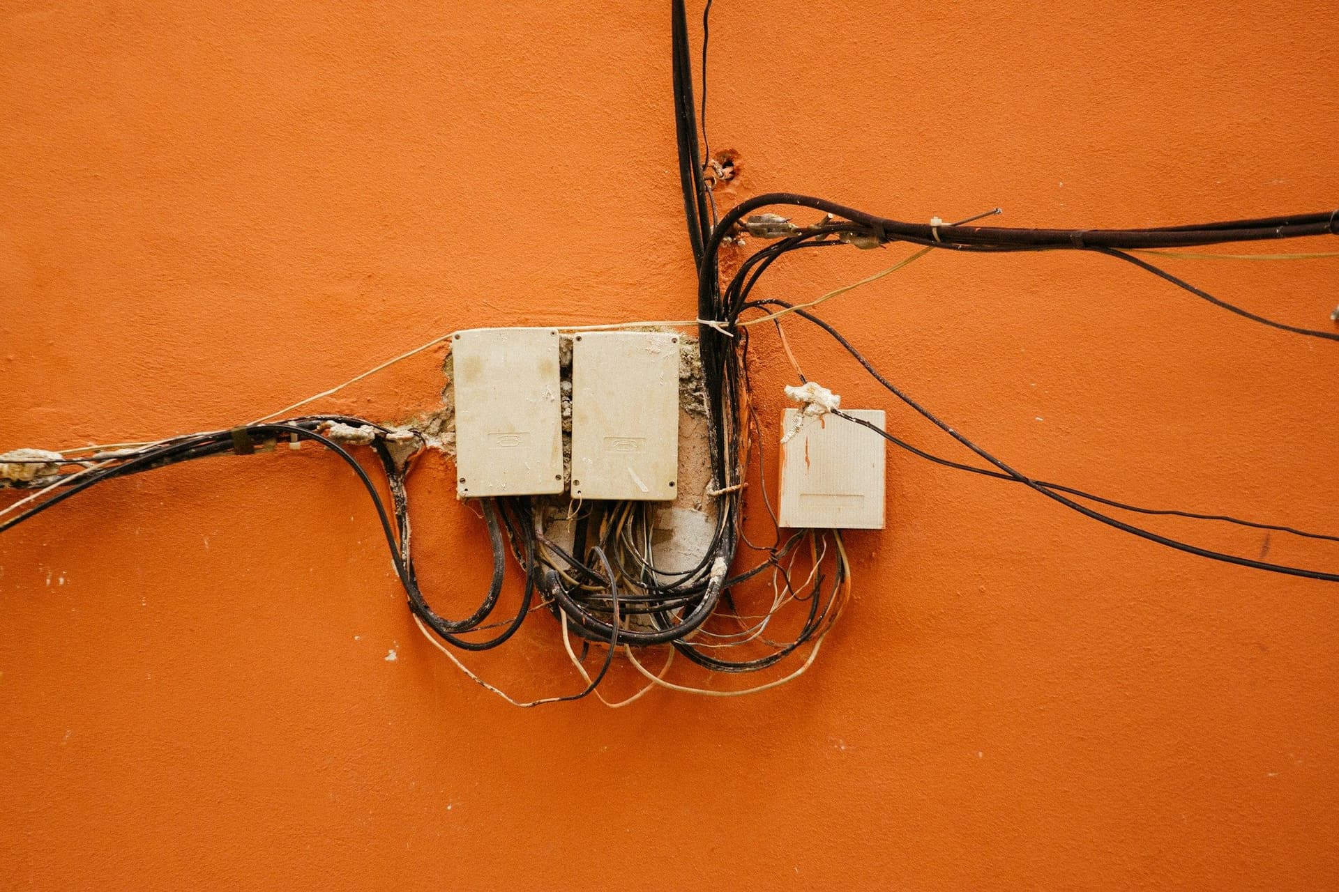 Tangled old cables running to small junction boxes on an orange wall