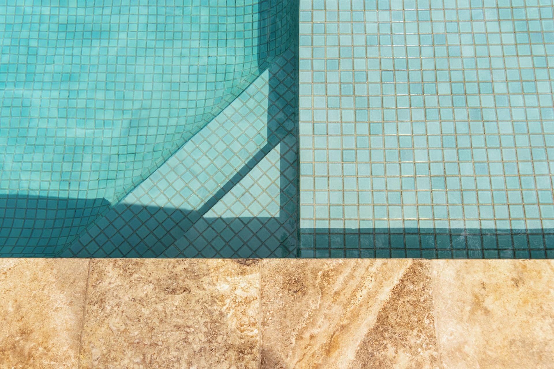 Tiled pool steps and ledge beside travertine coping stones in clear turquoise water