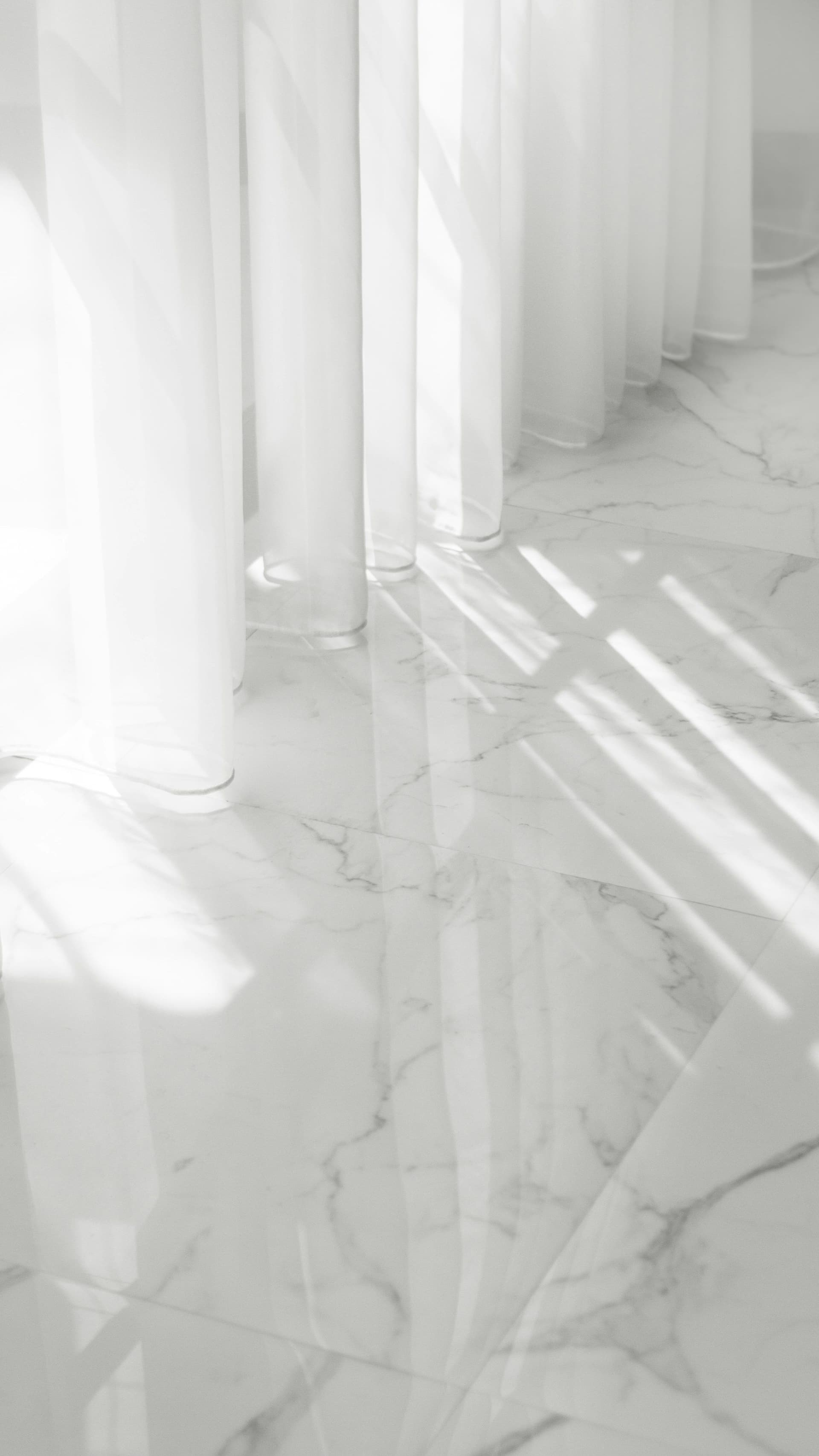 Glossy white floor tiles with fine gray veining beside sheer white curtains in a bright room