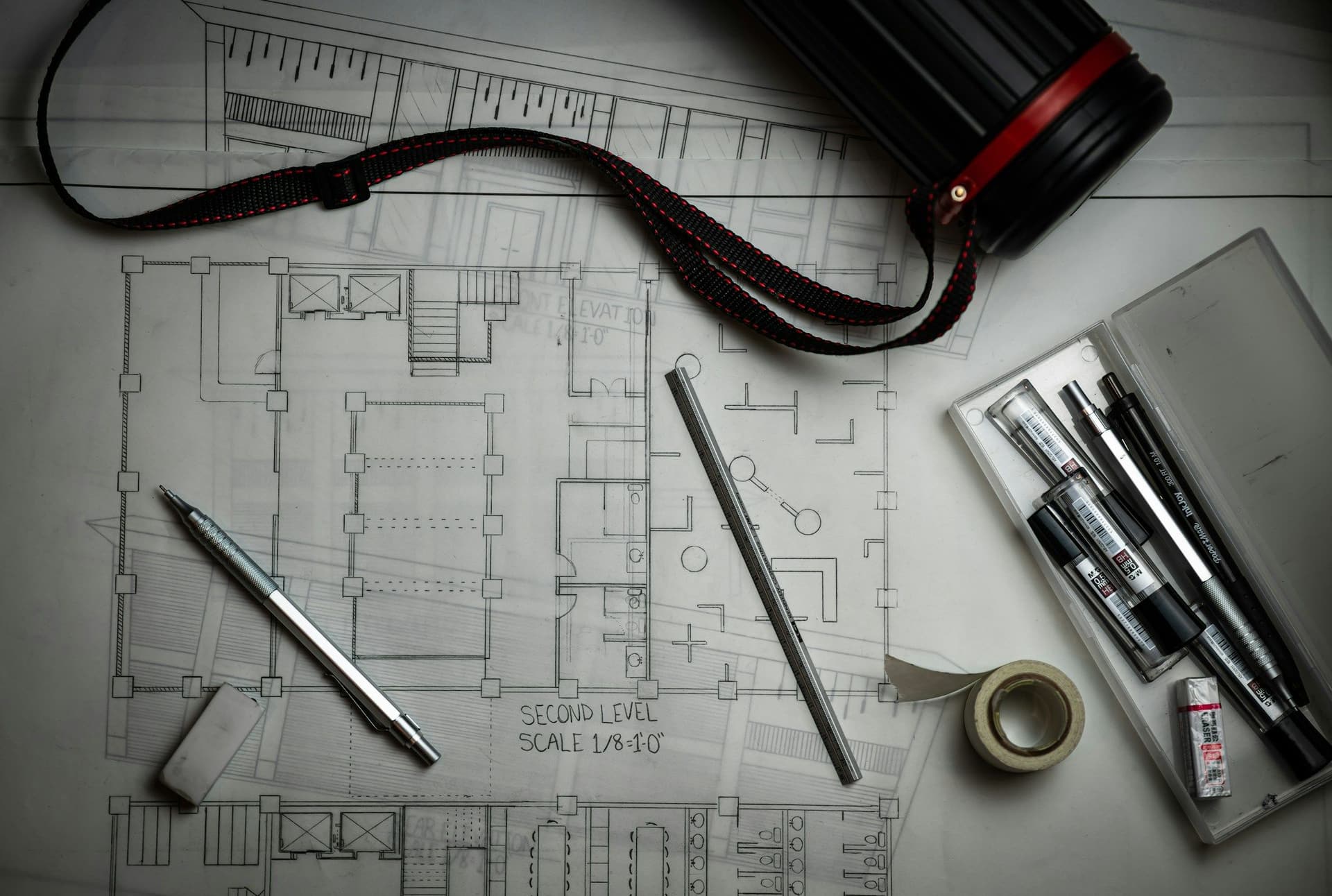 Architectural floor plans on a table with drafting pencils, an eraser, masking tape and a plan tube
