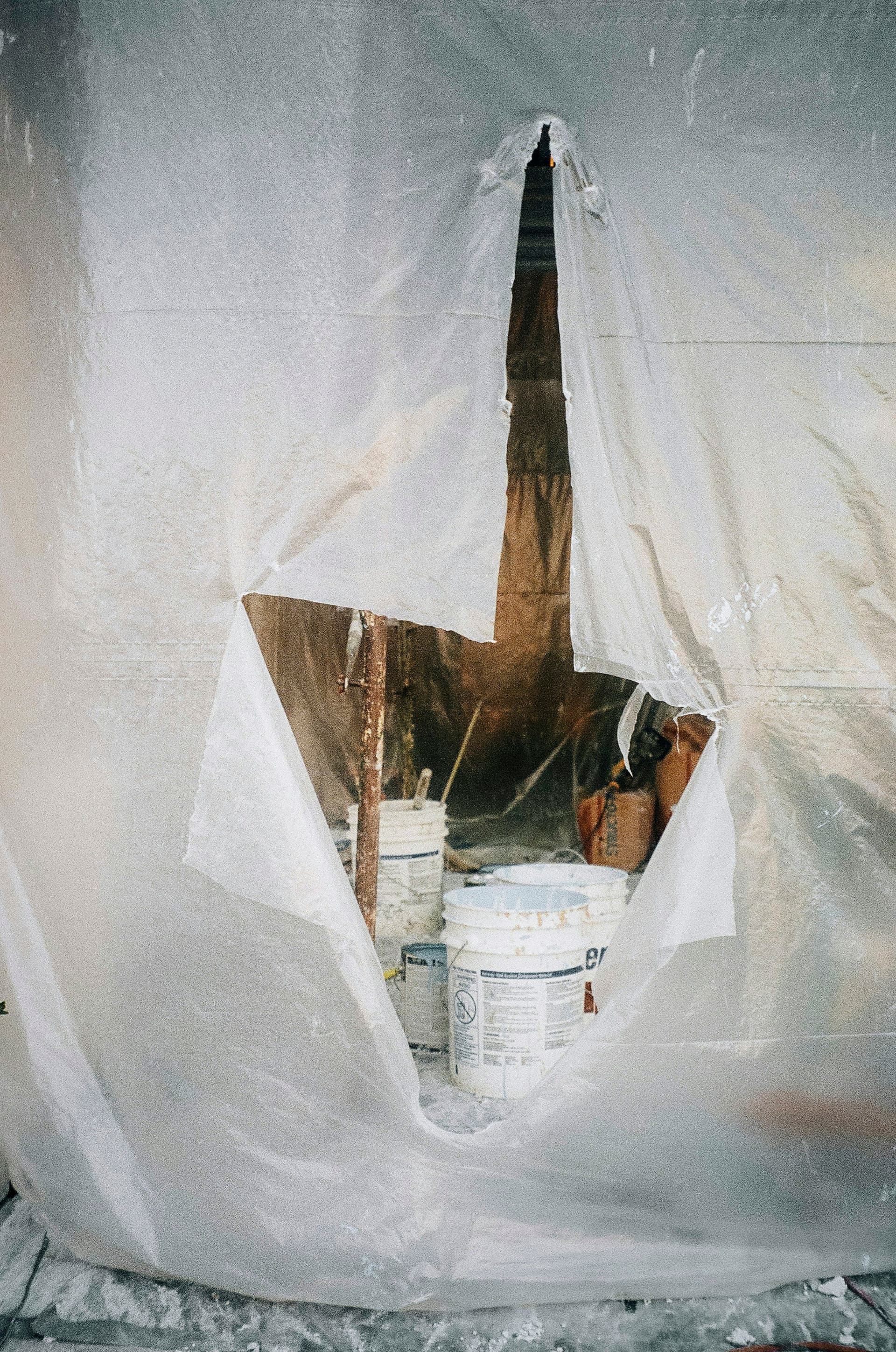 A plastic dust sheet sealing off a work area, with paint buckets visible through an opening