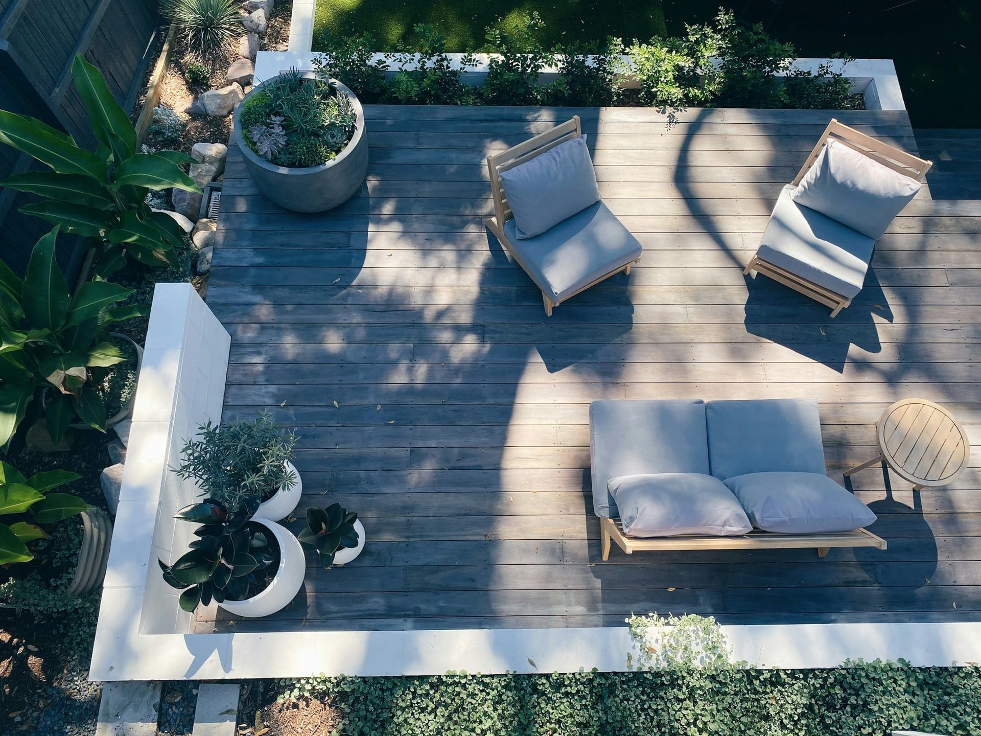 Aerial view of a dark wood deck terrace with lounge chairs, planters and white edging