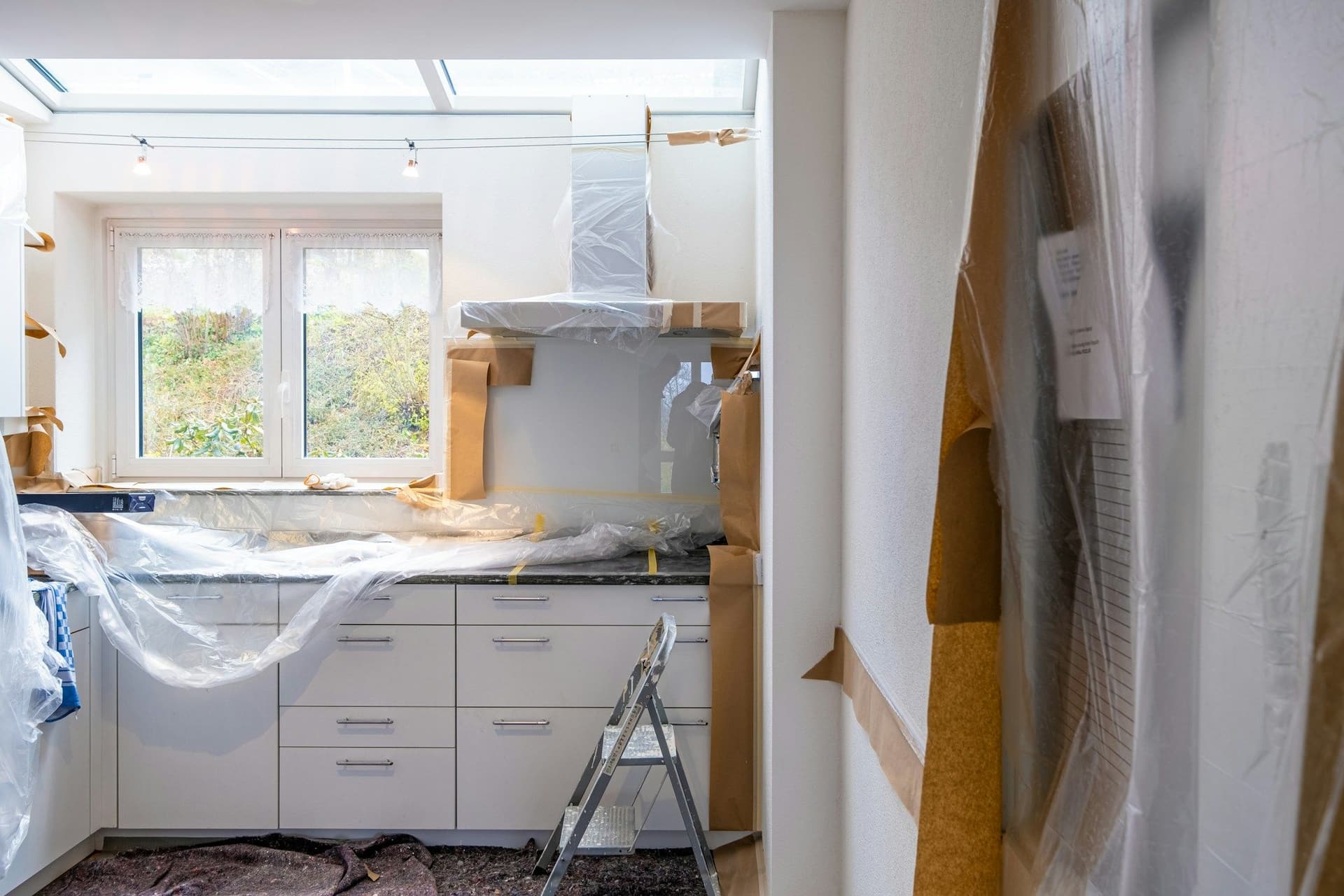 A kitchen mid-renovation with white base cabinets in place, plastic sheeting over the work and a stepladder