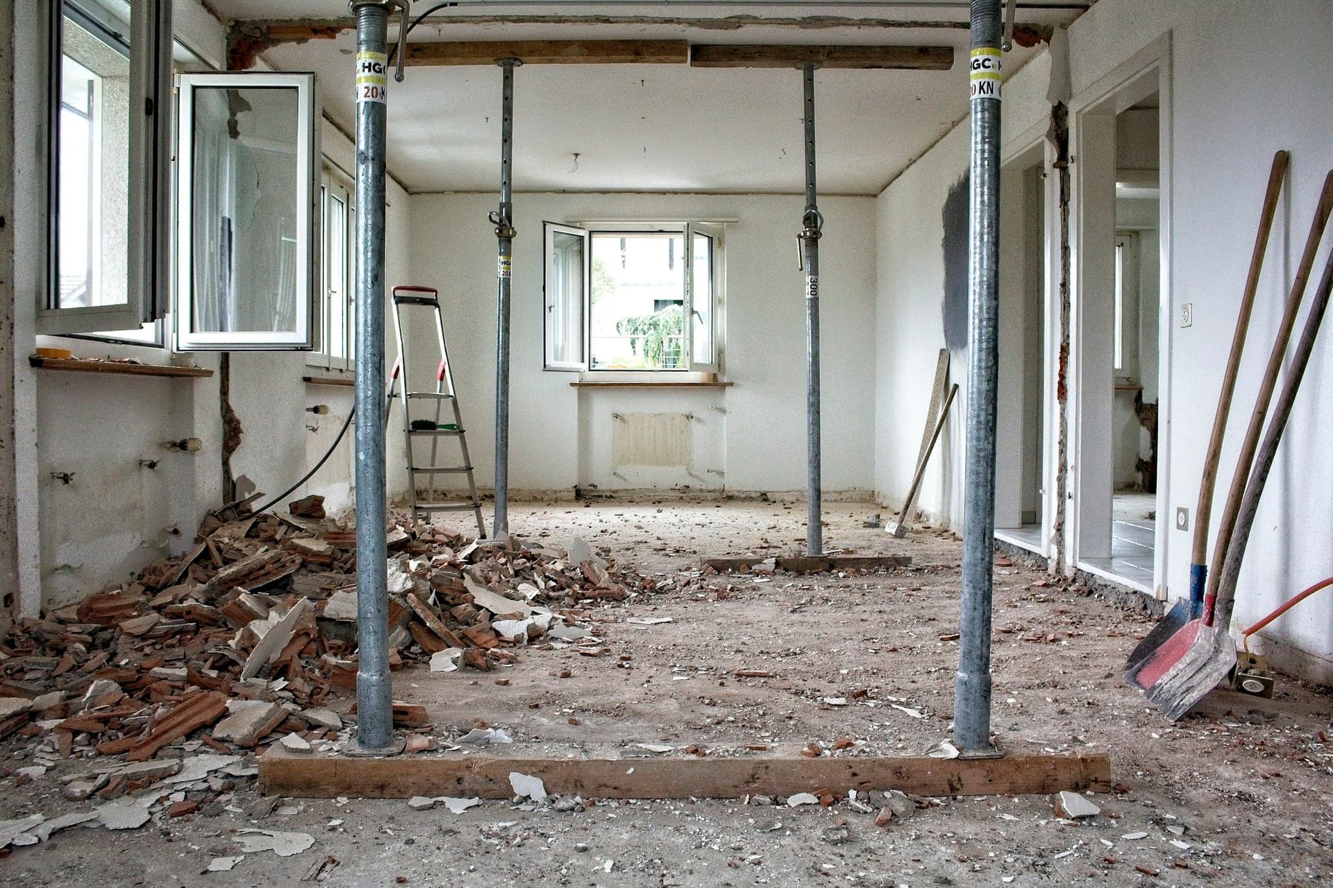 A room stripped back for renovation, with temporary steel props holding the ceiling and debris on the floor