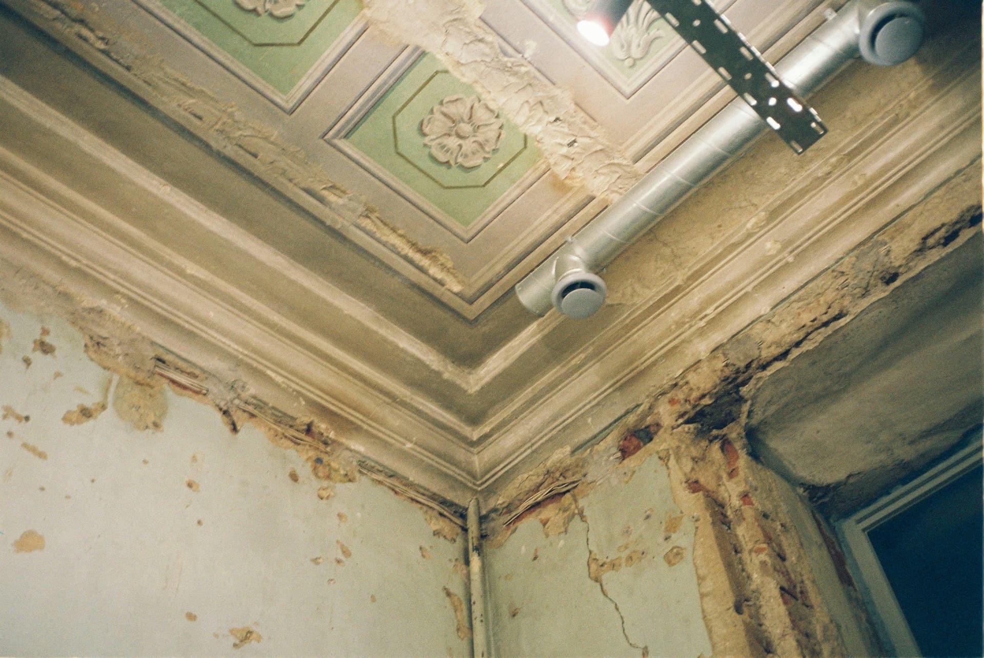 Corner of an ornate ceiling with brown stains and flaking plaster along the wall joint