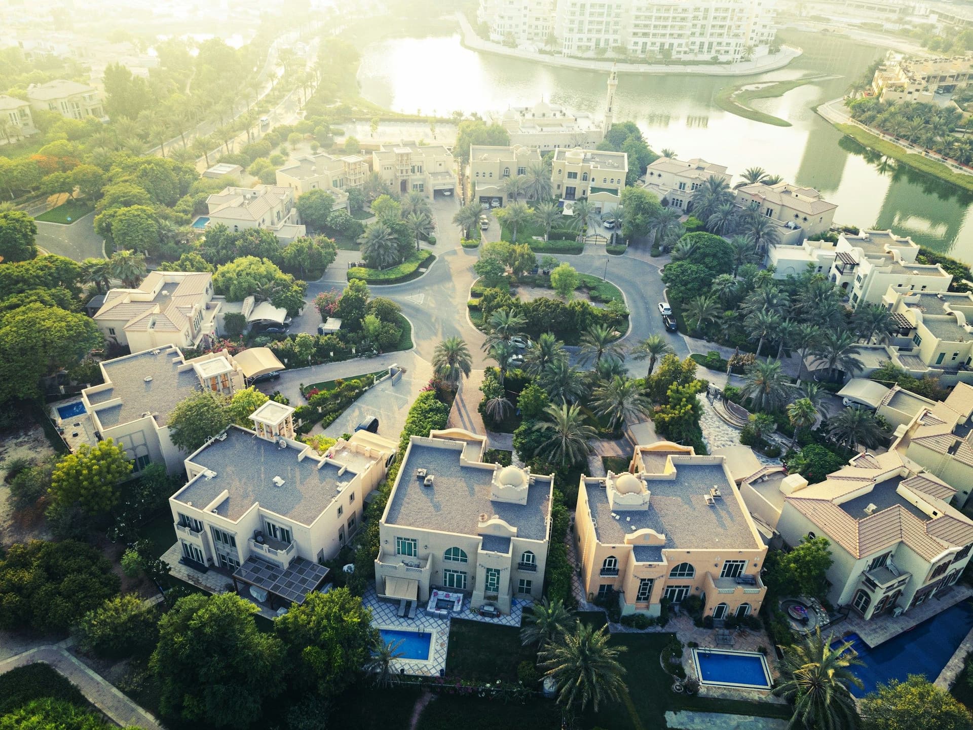 Aerial view of a Dubai villa community with private pools, palm trees and a lake