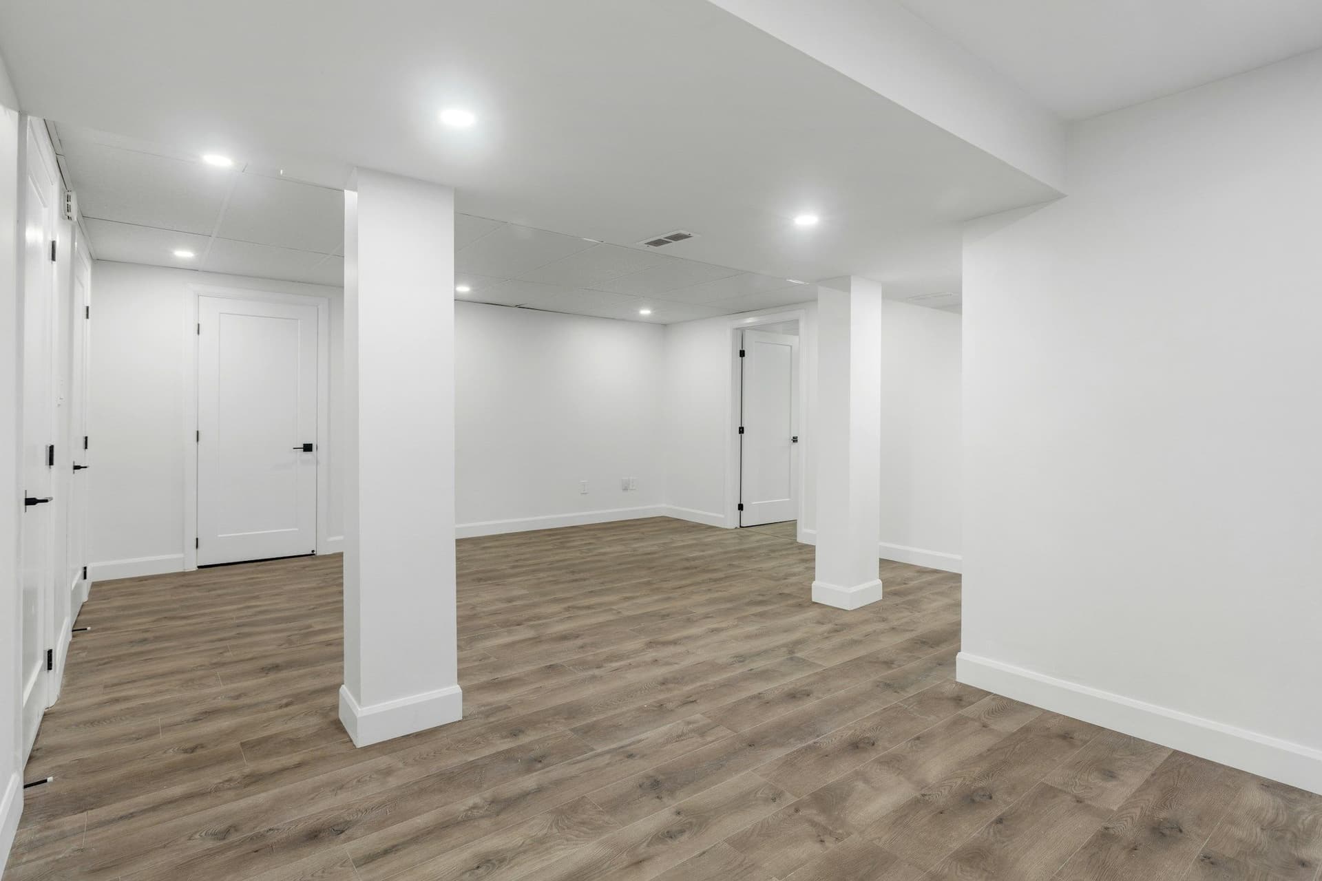 A freshly finished room with white walls, recessed lights and a wood-look floor