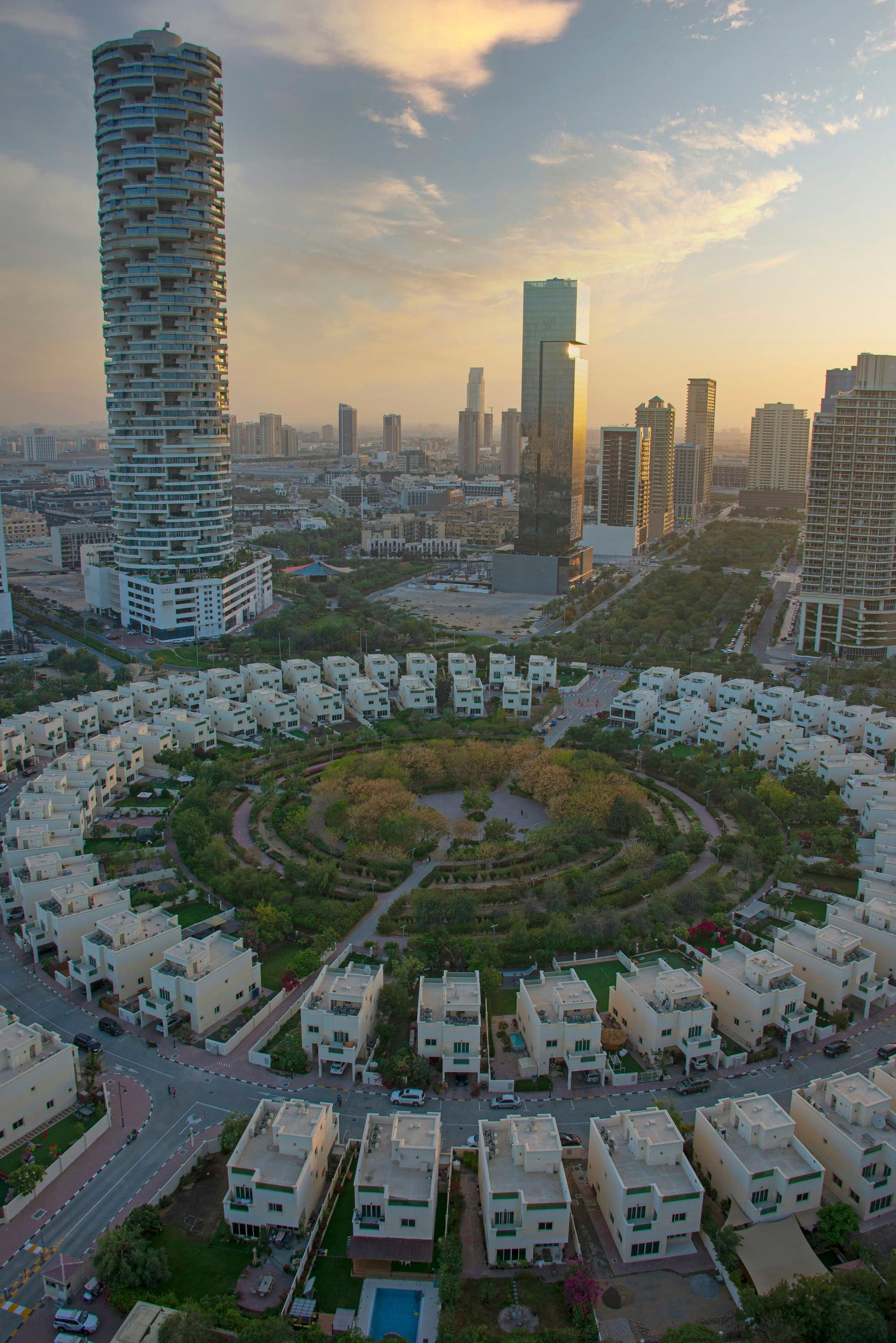 Aerial view of a circular villa community in Dubai with towers behind at dusk