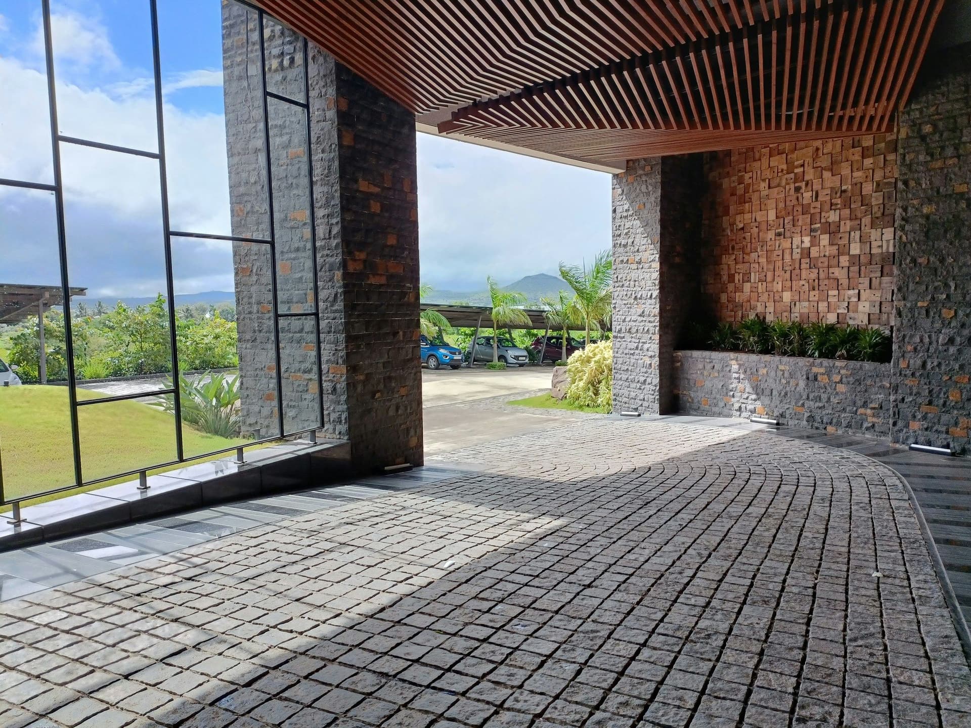 Covered entrance drive paved in dark interlocking blocks beside stone walls and a wood slat ceiling