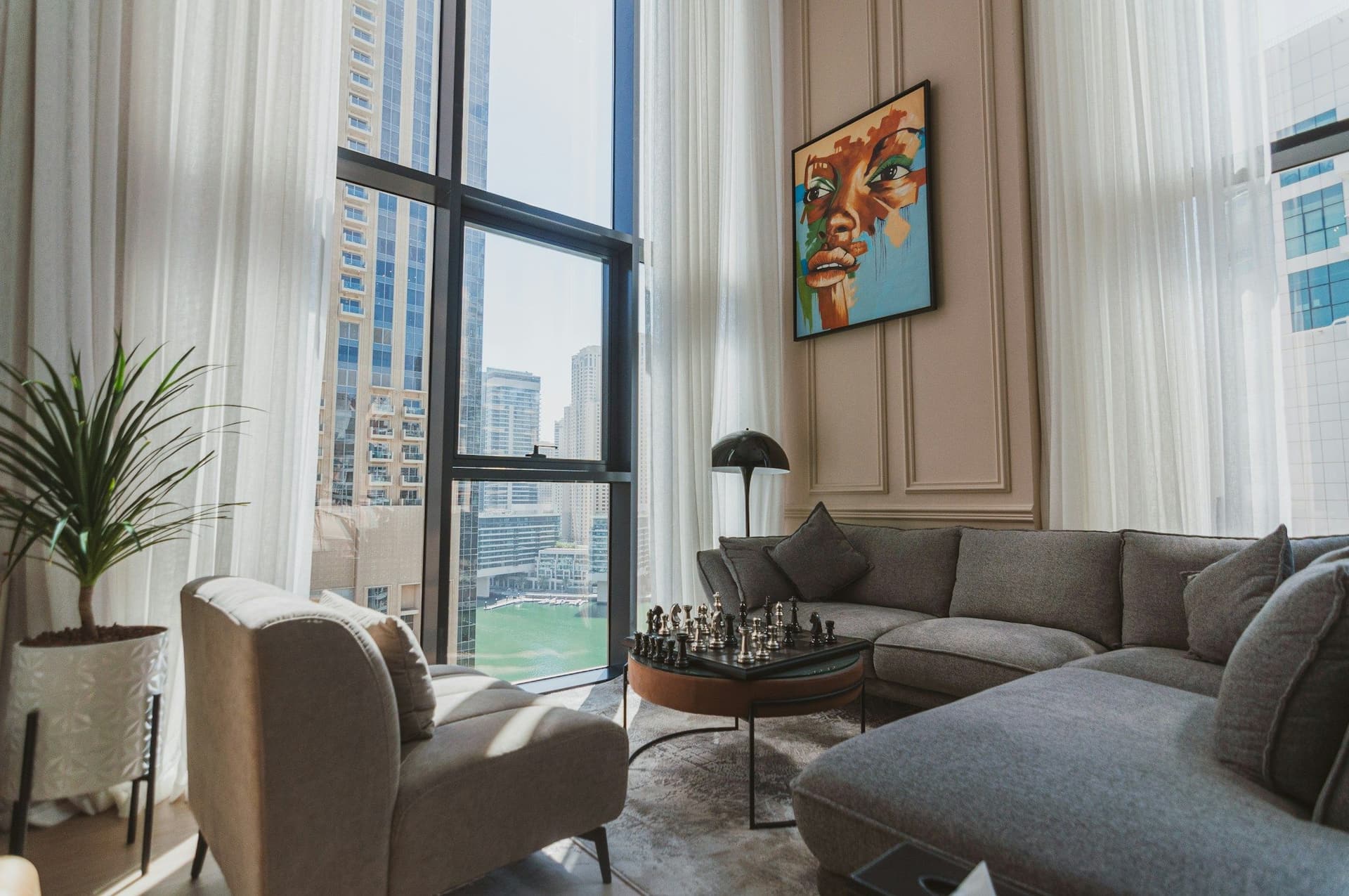 Bright living room with a gray sectional sofa, an armchair and tall windows looking out over high-rise towers