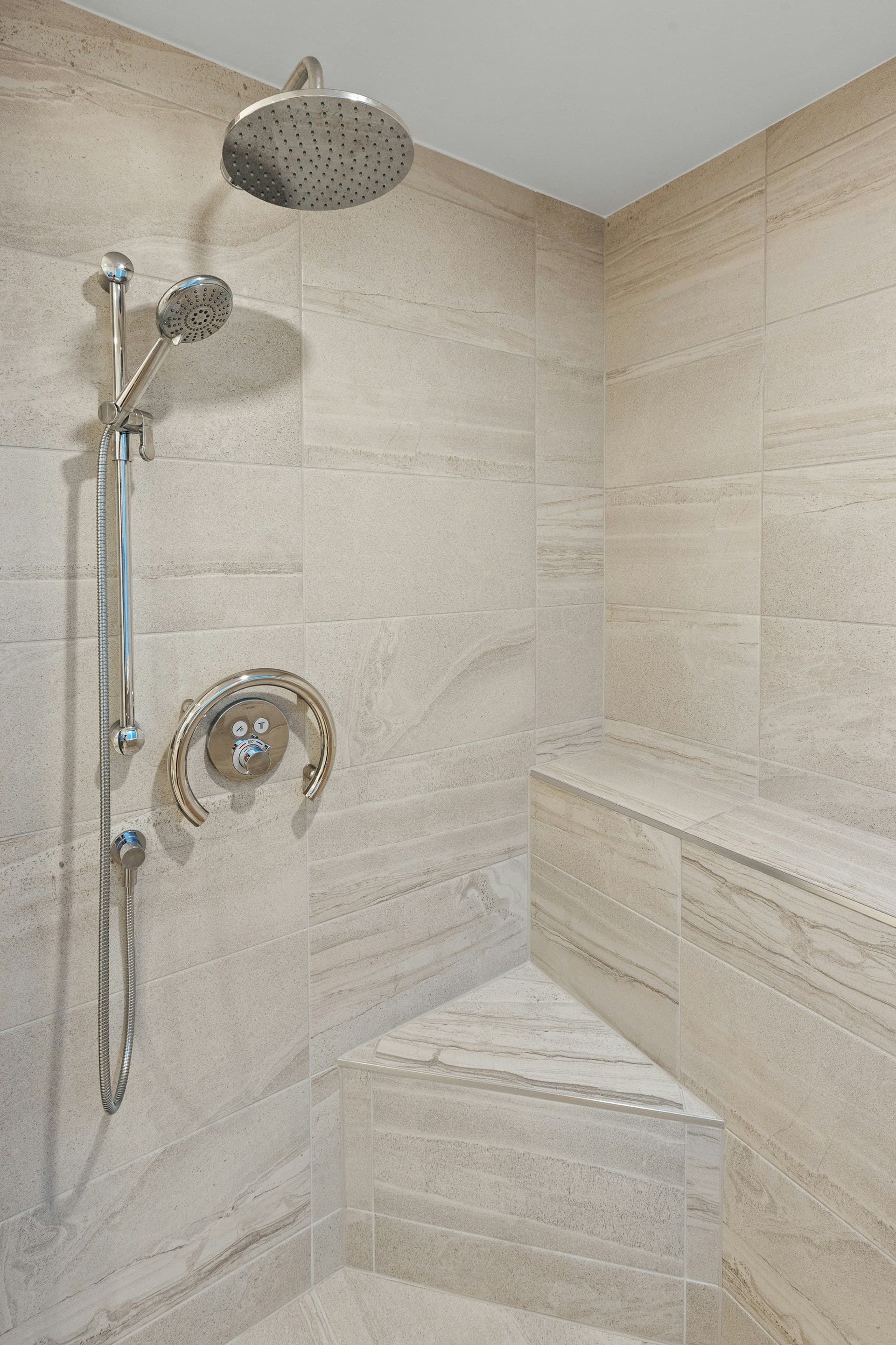 Tiled shower with a corner seat, a hand shower on a slide bar and a ring-shaped grab handle