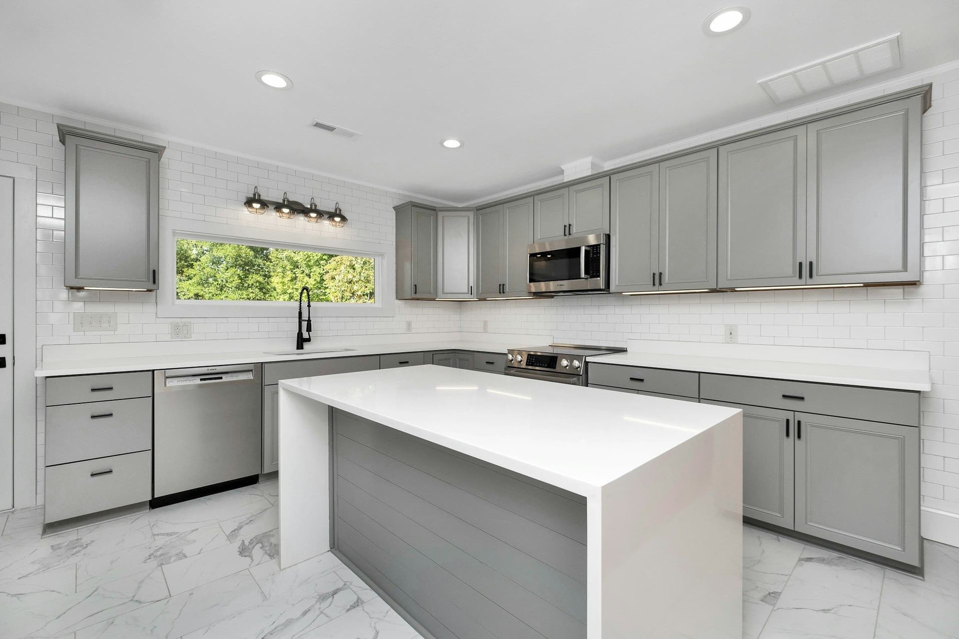 Kitchen with gray painted cabinets, a white waterfall island and a marble-look tiled floor