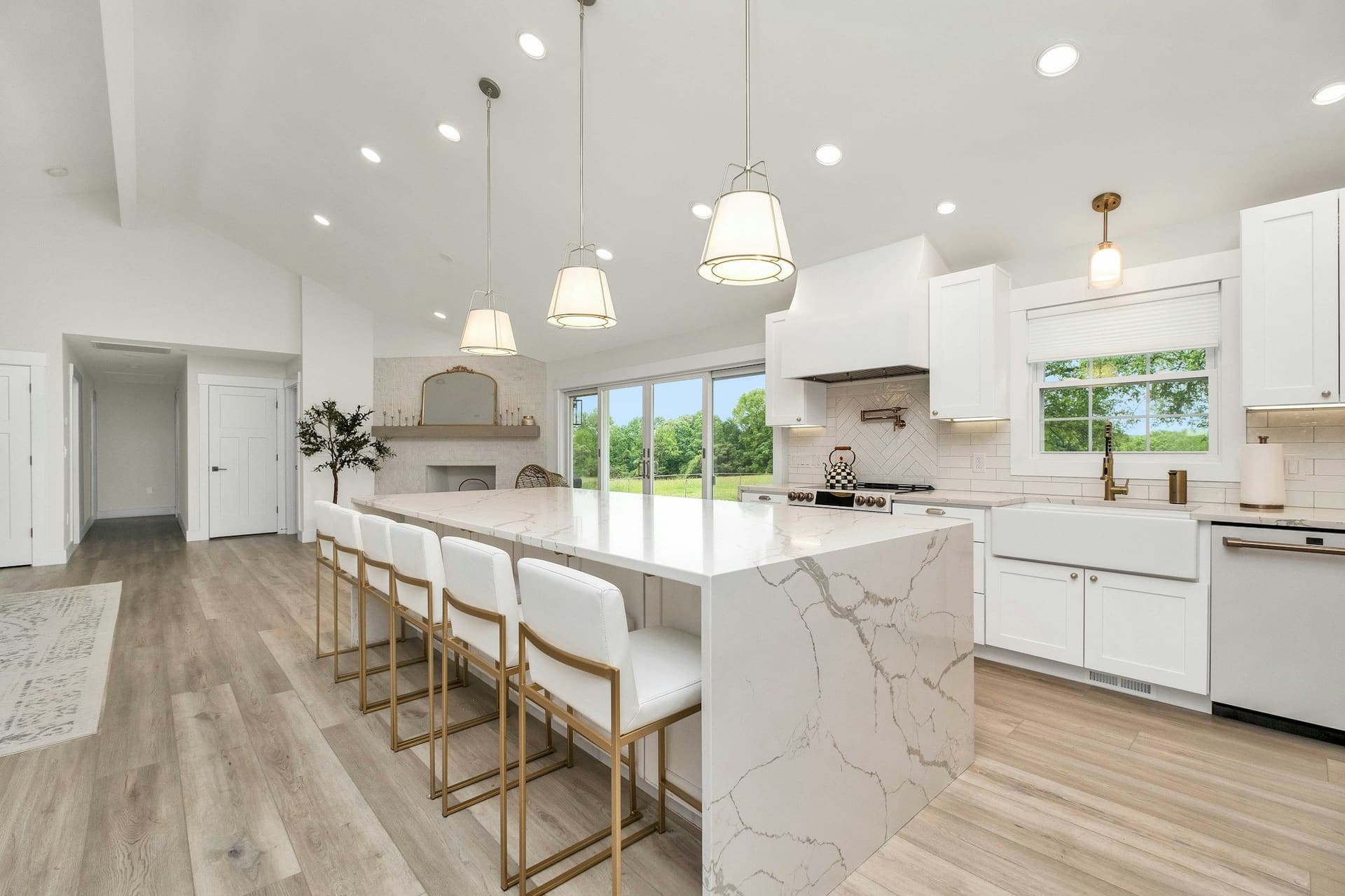 Large white kitchen with a marble-look waterfall island, bar stools, pendant lights and a wood-look floor