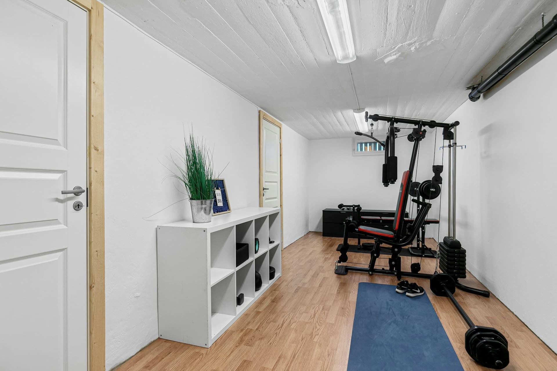 Home gym in a white room with a wood floor, a weight bench, a cable machine and a blue mat
