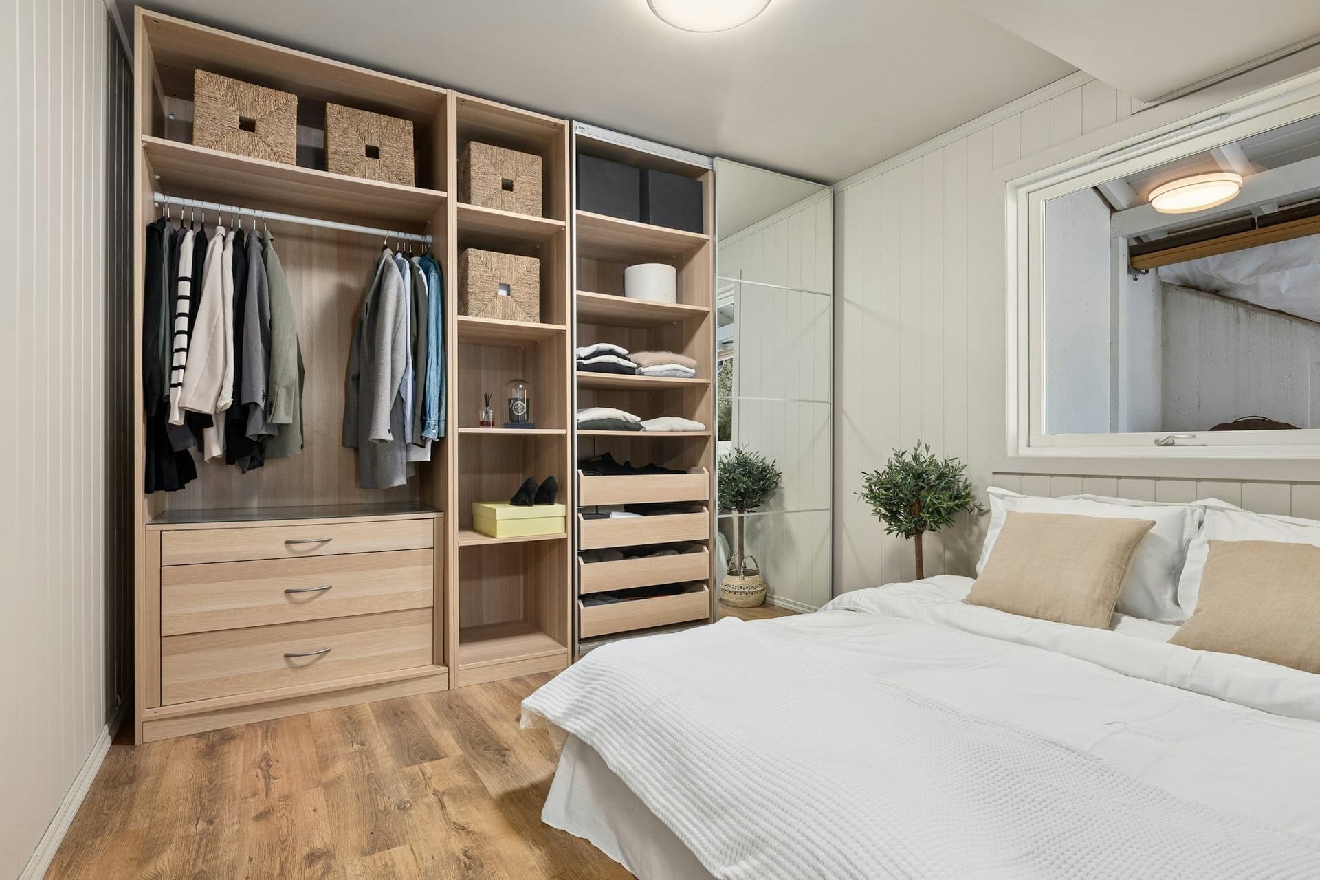 Bedroom with a built-in light wood wardrobe, a made bed, a wood-look floor and a round ceiling light
