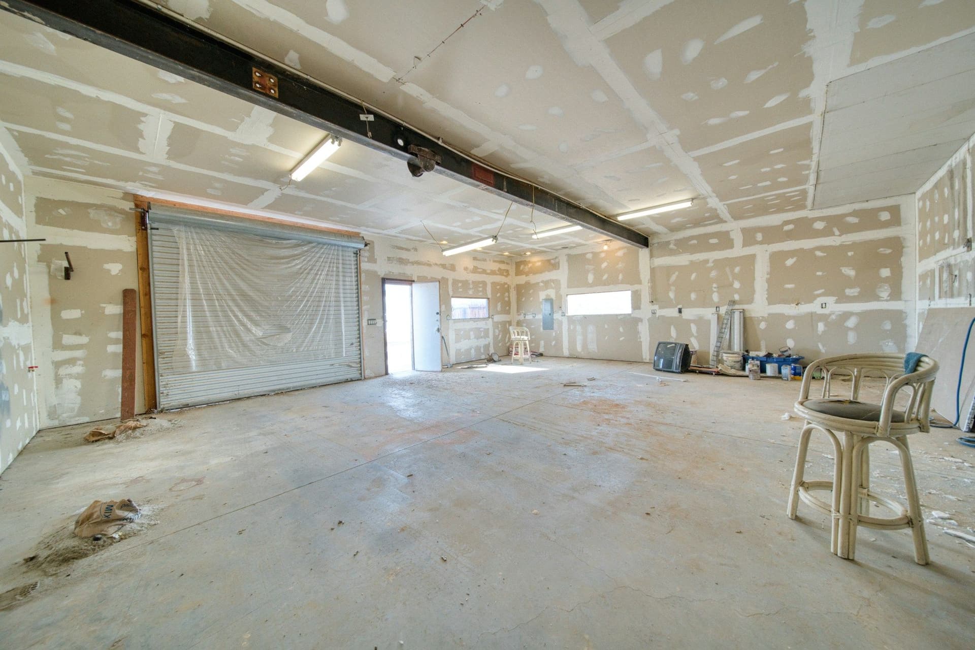 Bare room with drywall joints taped and filled across the walls and ceiling, a stool in the foreground
