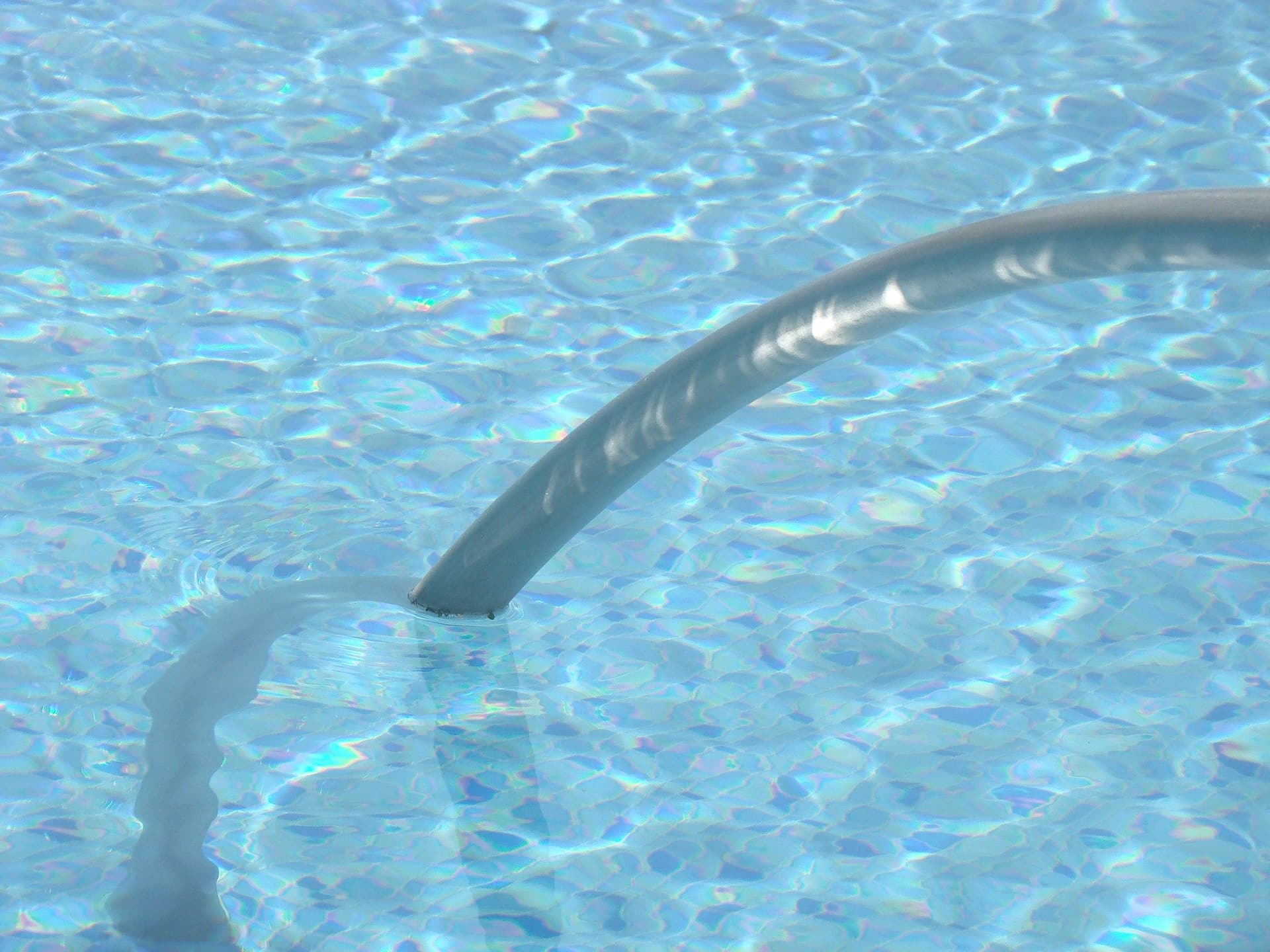 A gray cleaning hose trailing through clear rippling pool water