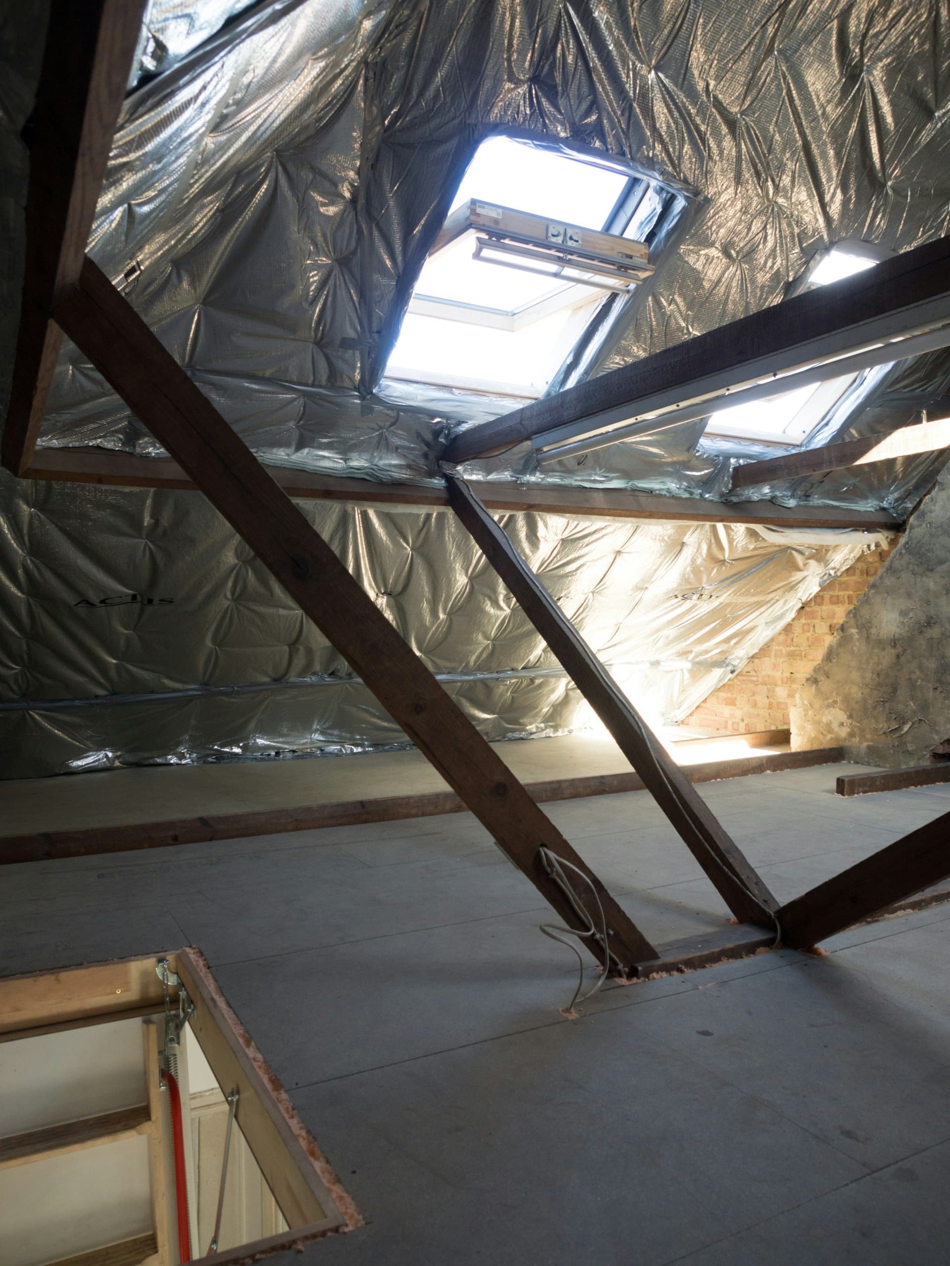 Attic roof space lined with reflective insulation between timber rafters, with skylights and a hatch in the floor