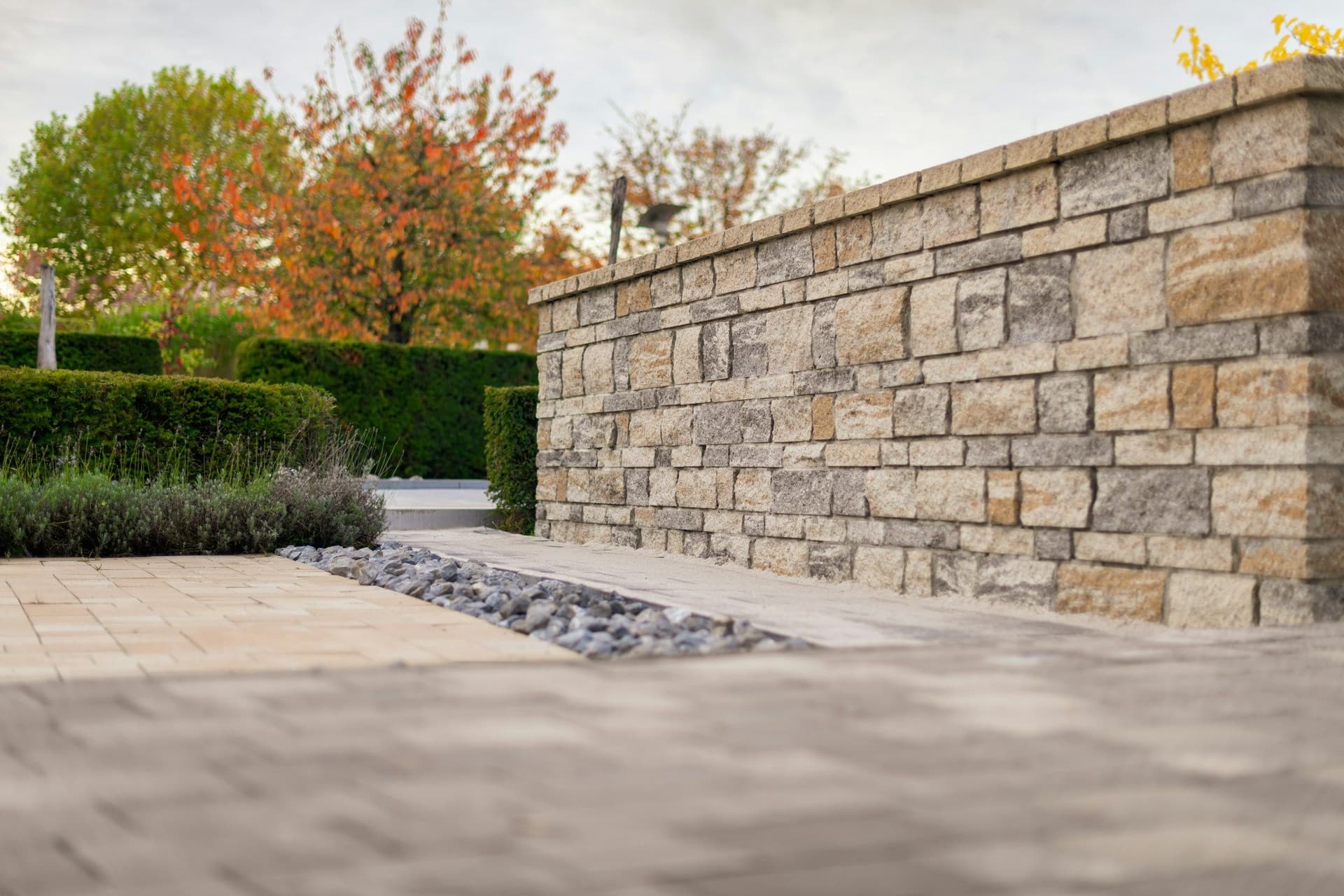 Low natural stone wall beside block paving and trimmed hedges in soft light