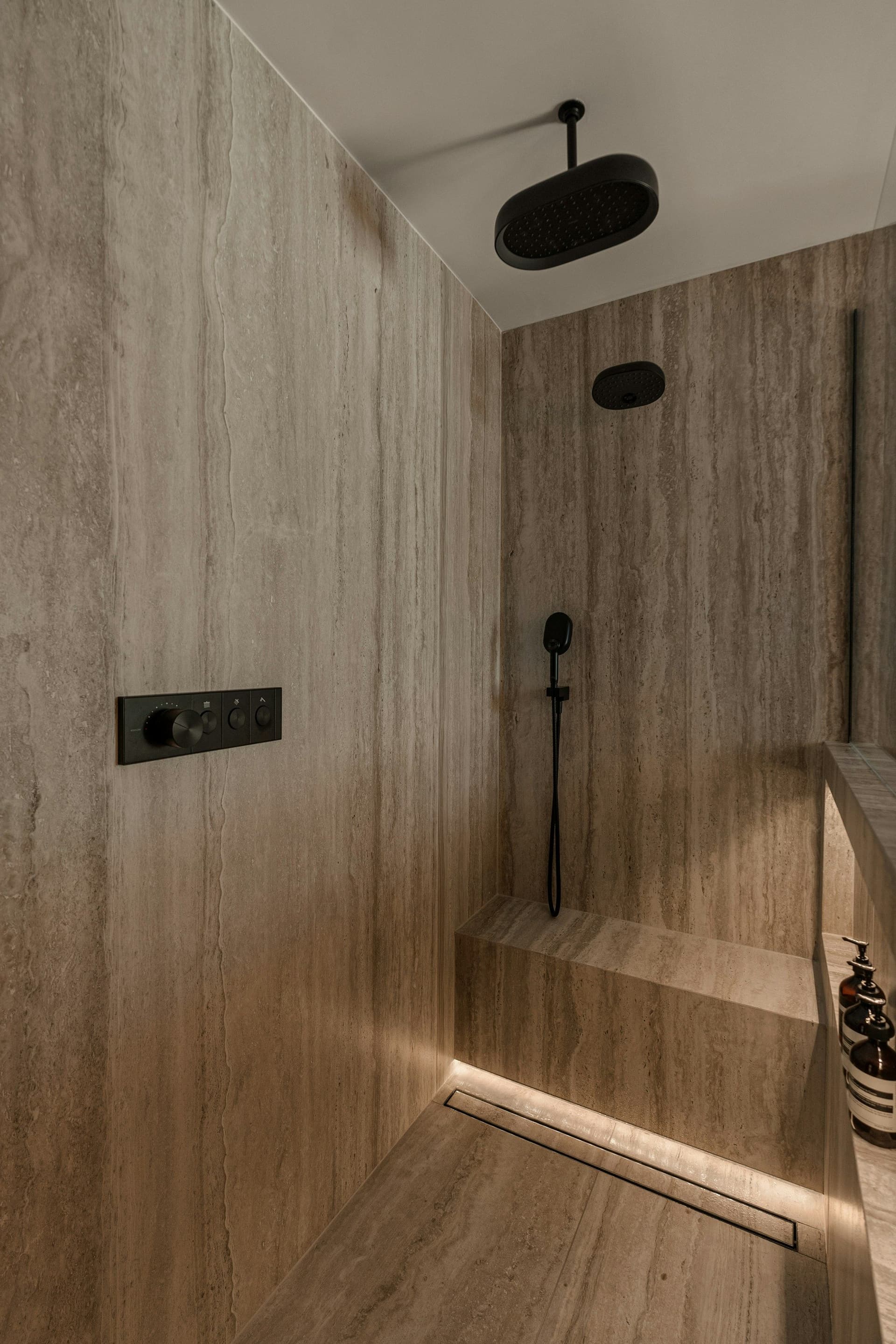 Walk-in shower lined in stone-look tile with a bench, a ceiling rain head and a linear drain