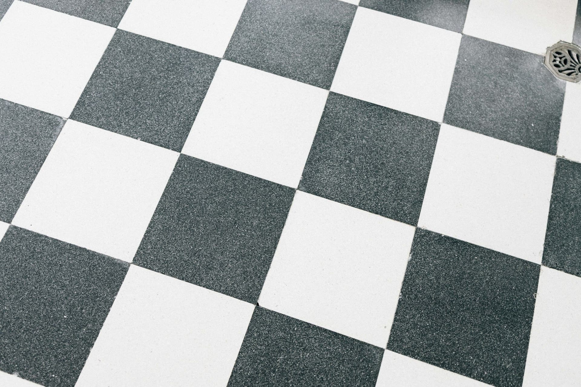 Black and white square tiles laid on the diagonal, with a floor drain in the corner