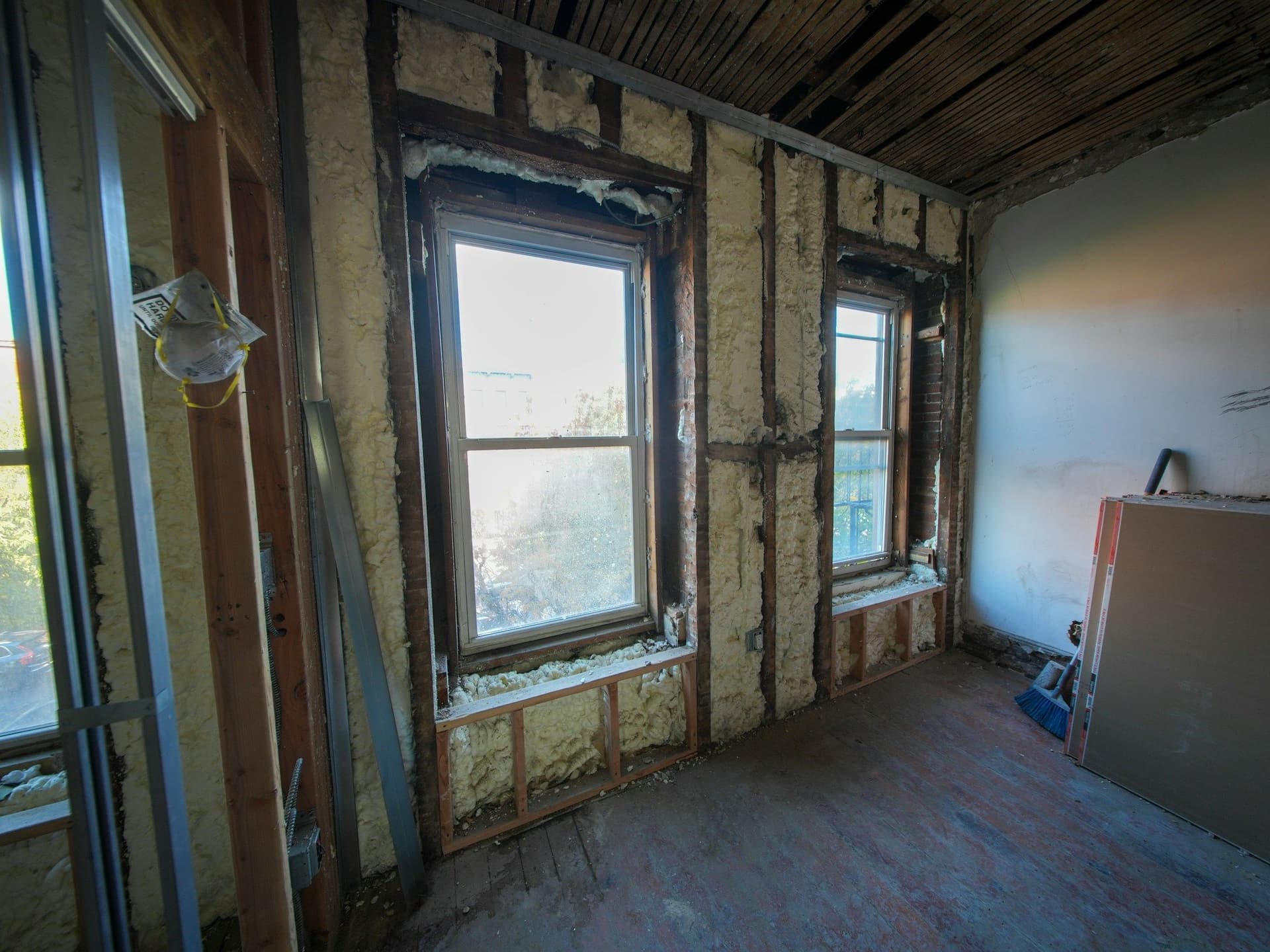 Room stripped back to wall studs and insulation, with two windows and a bare wood floor