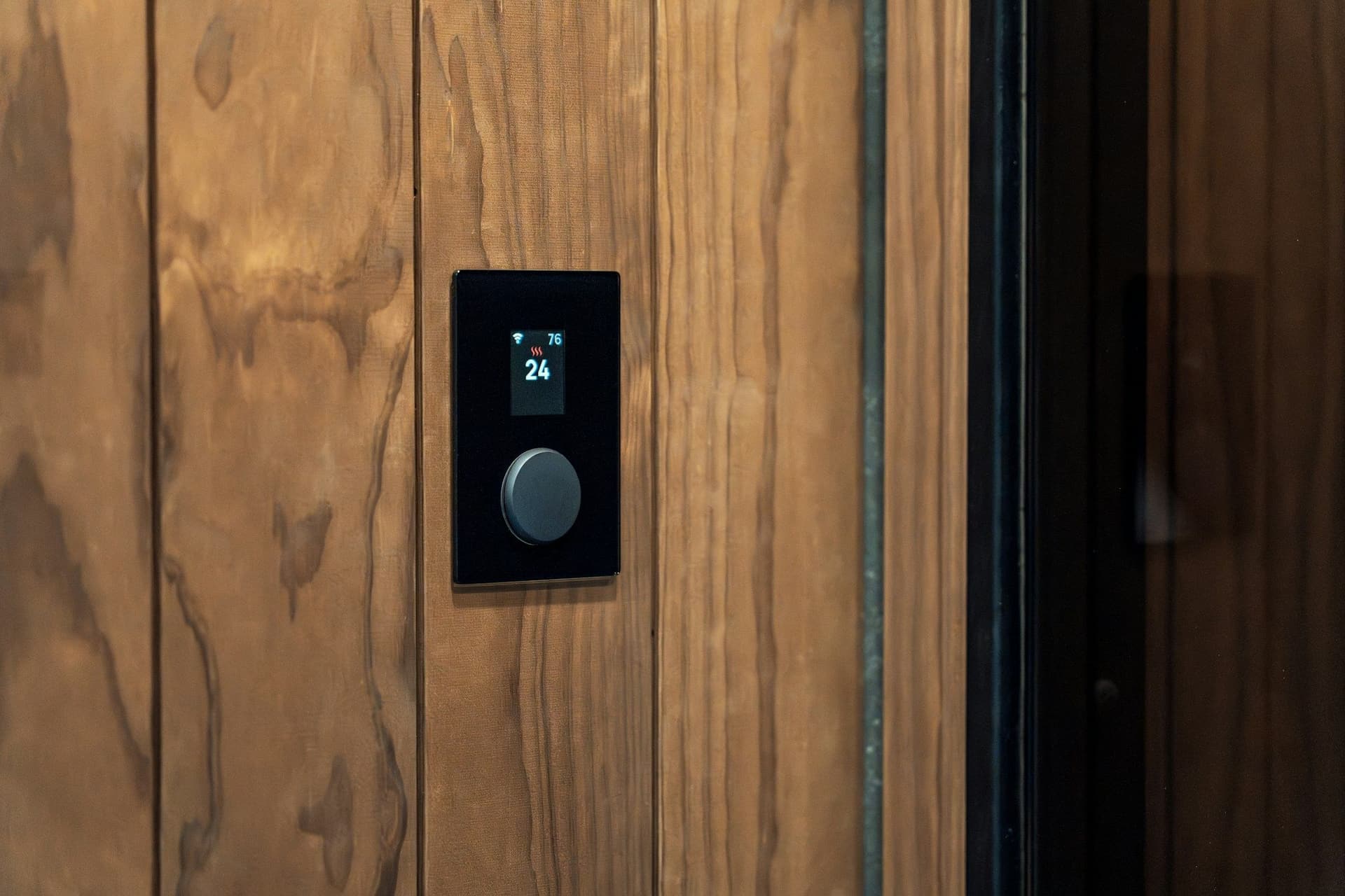 Black wall control panel with a temperature display and a round dial set into dark wood paneling