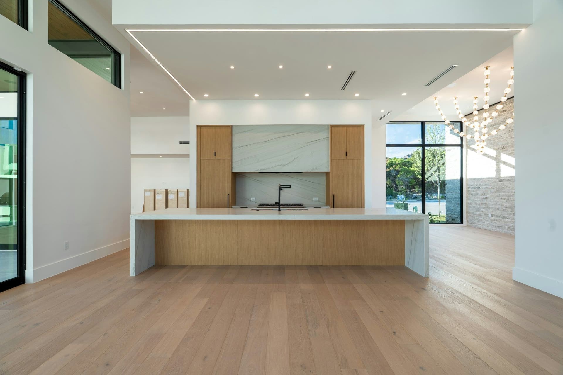 Open living and kitchen space with a long wood-faced island, a wide-plank floor and large glass doors
