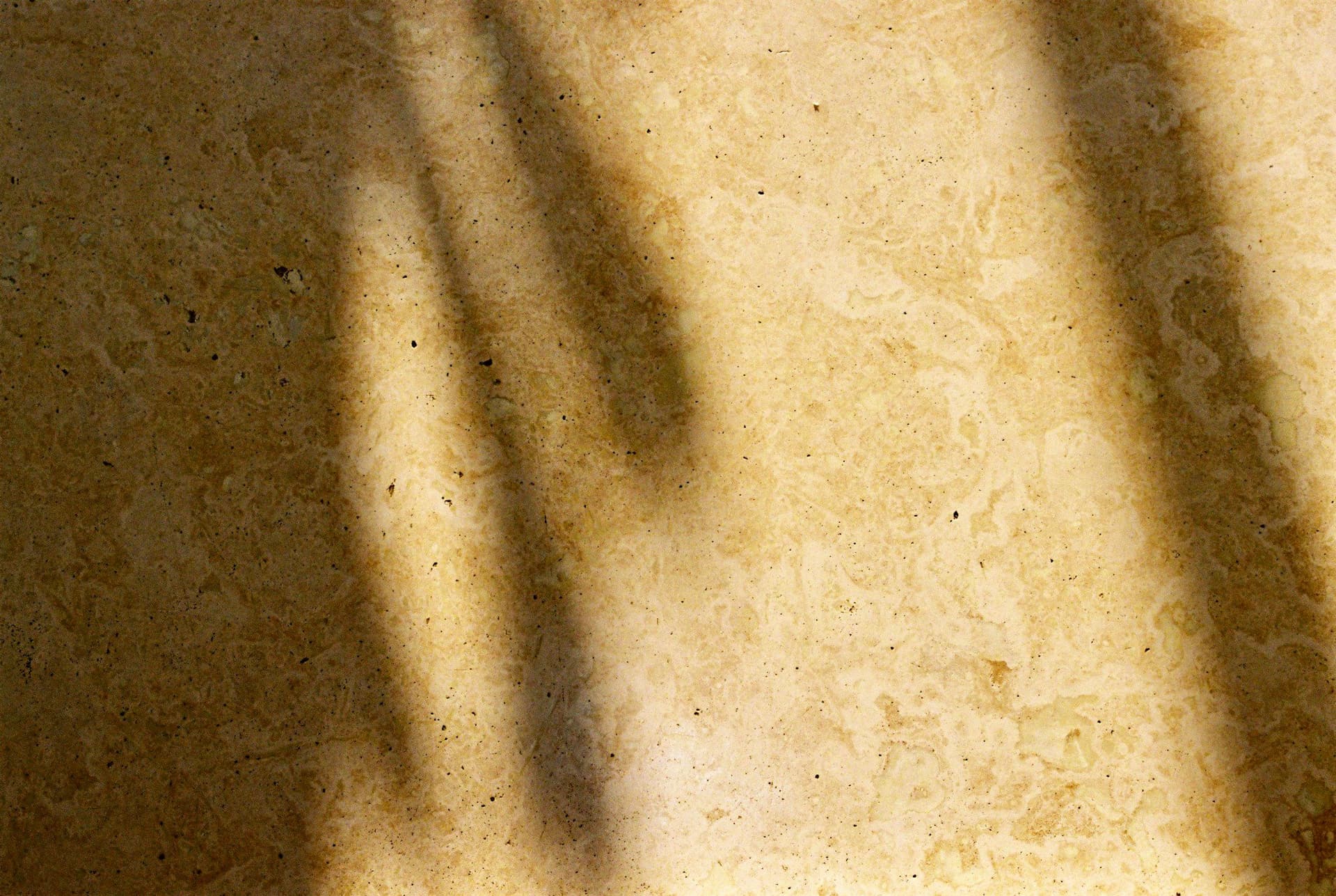 Cream stone floor with a mottled surface and soft leaf shadows from a nearby window