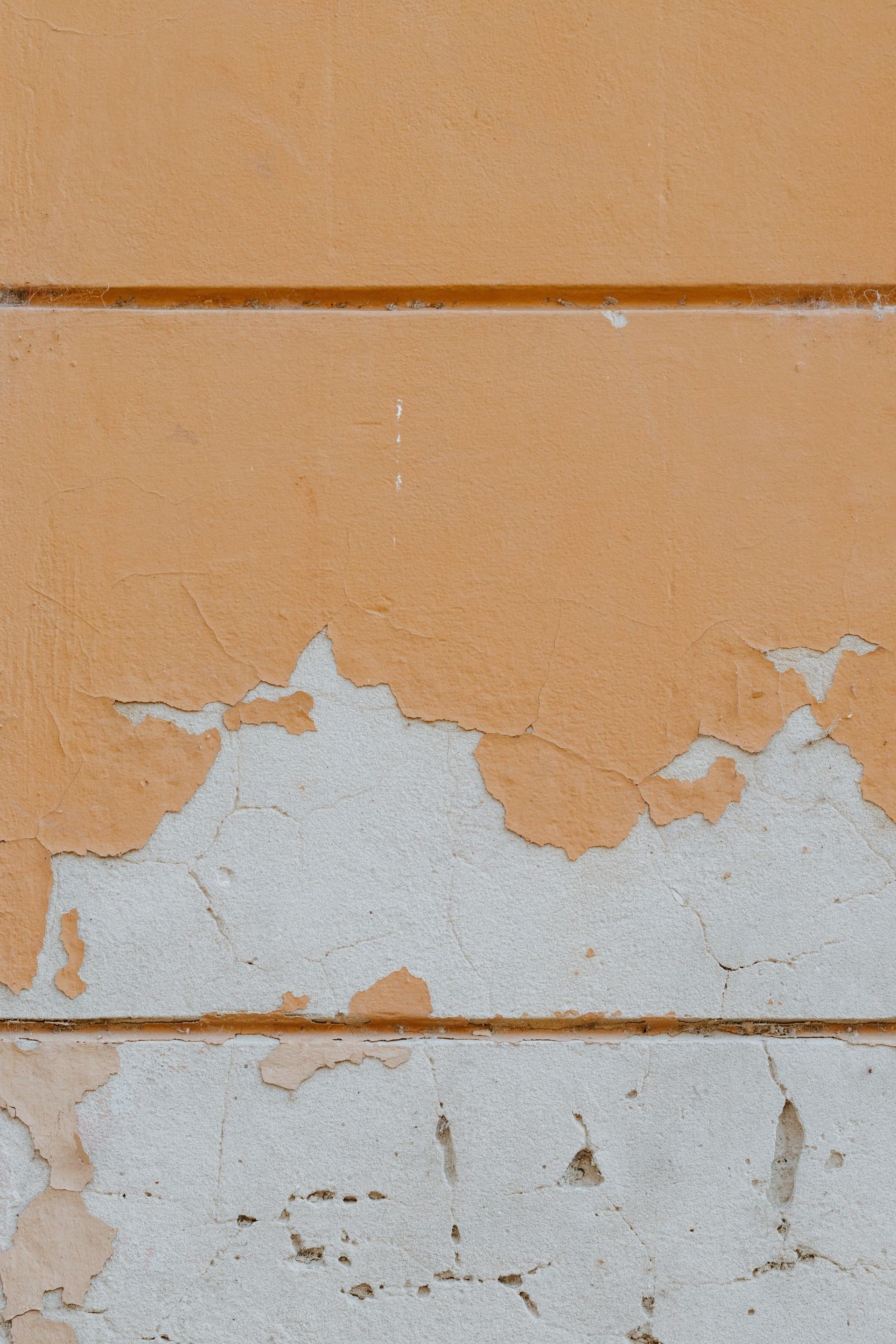 Peeling orange paint on a rendered wall, with bare gray plaster showing underneath